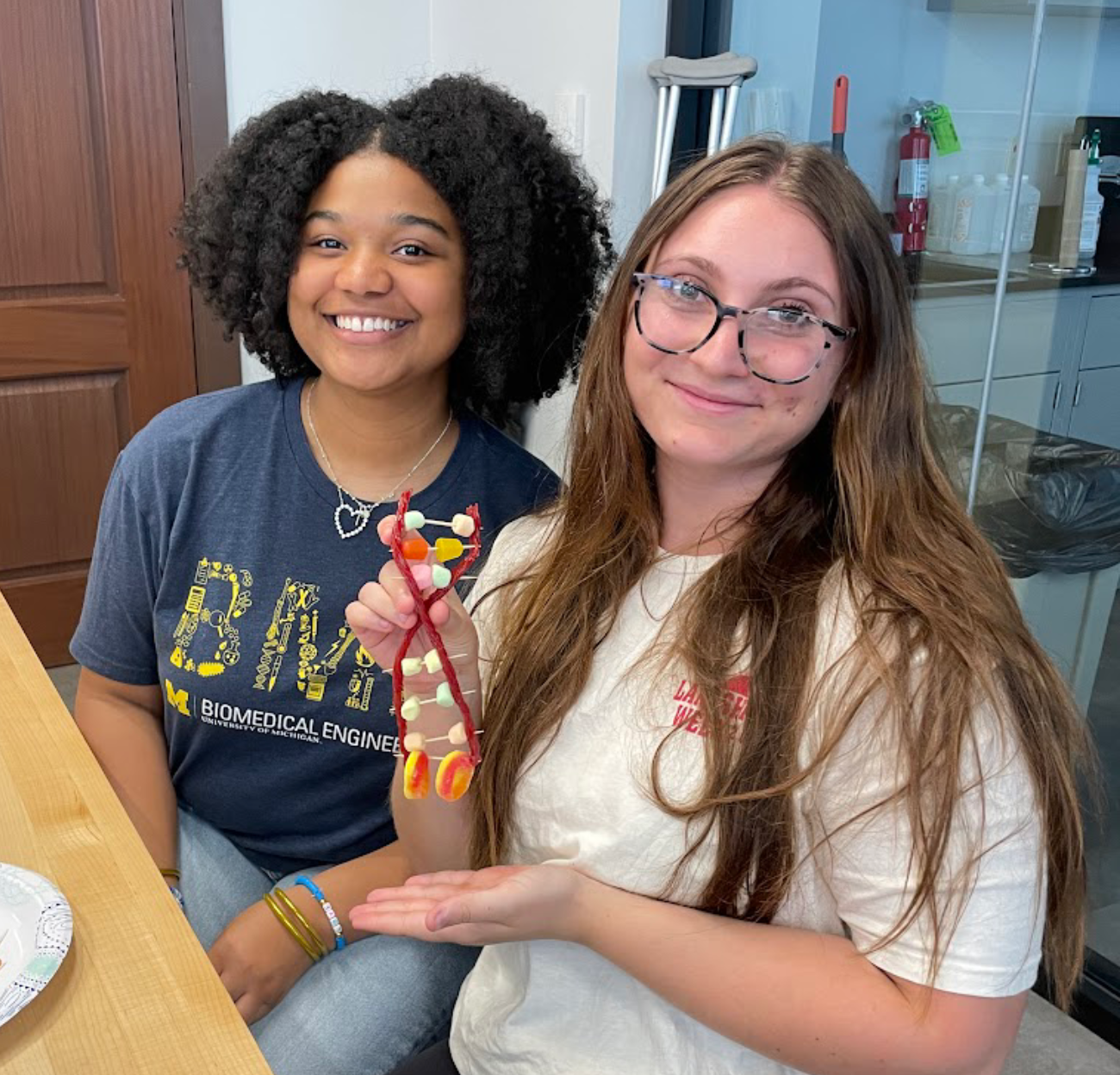 Two students hold up a DNA strand constructed of toothpicks and candy.