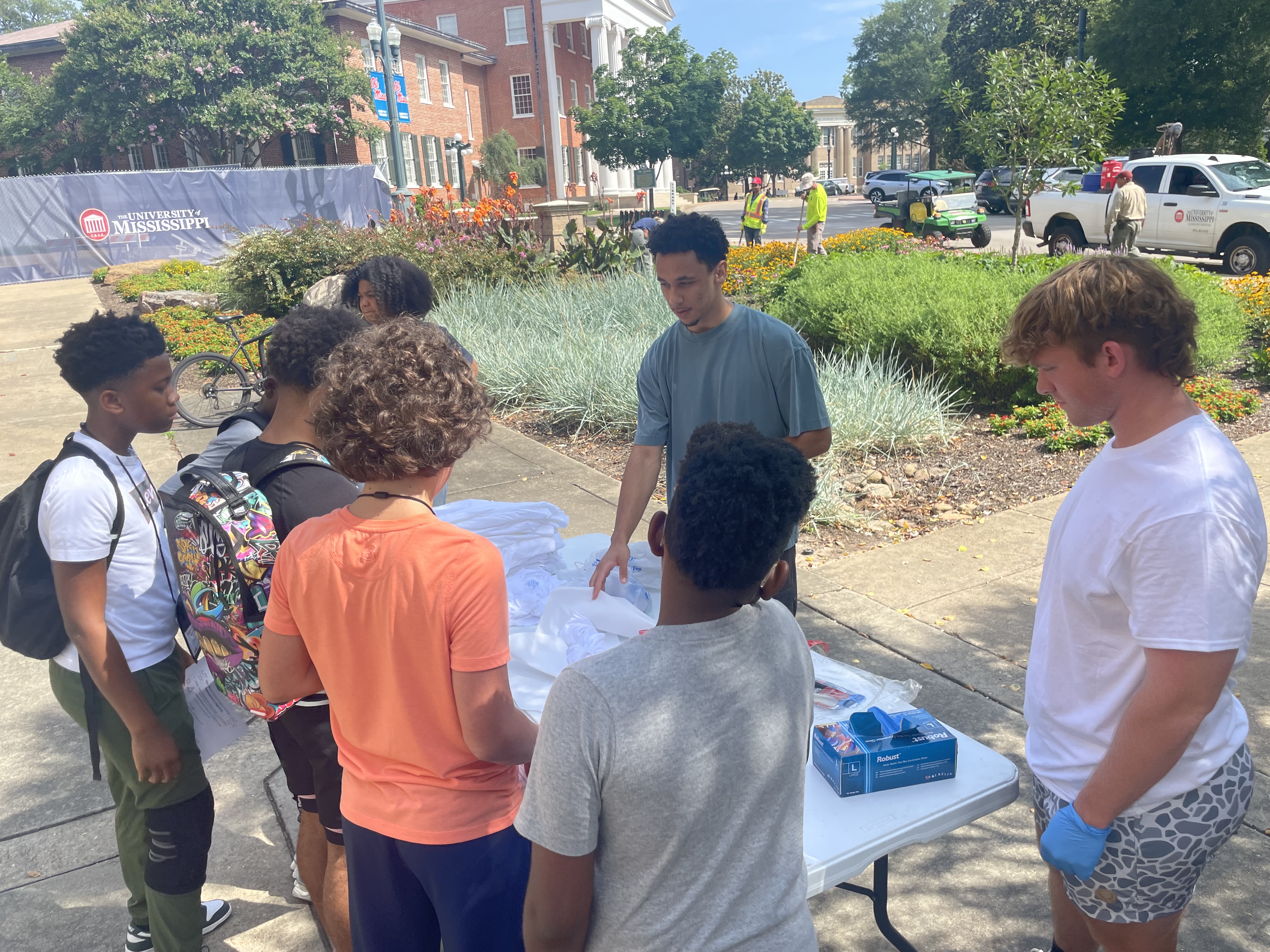 Two undergraduate students explaining a concept to a group of middle school students outside Brevard Hall.